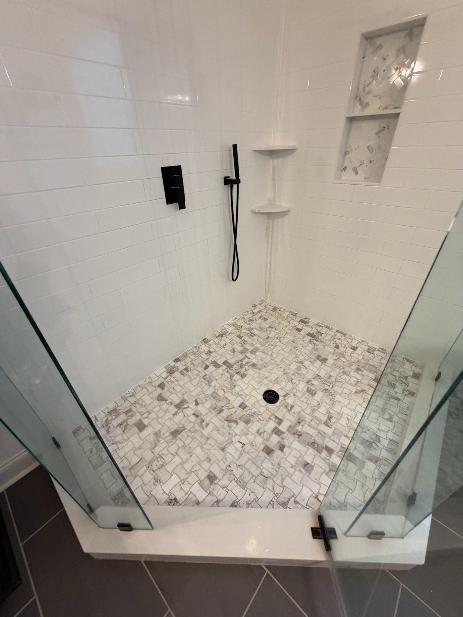 Elegant corner glass shower with white subway tiles, mosaic floor, and matte black fixtures.