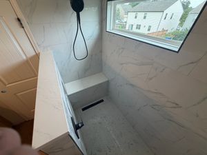 Luxurious walk-in shower with white marble-look porcelain tile walls and built-in bench.