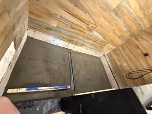 Shower floor installation with concrete base, wood plank walls, and a level tool on a partially completed tile project.