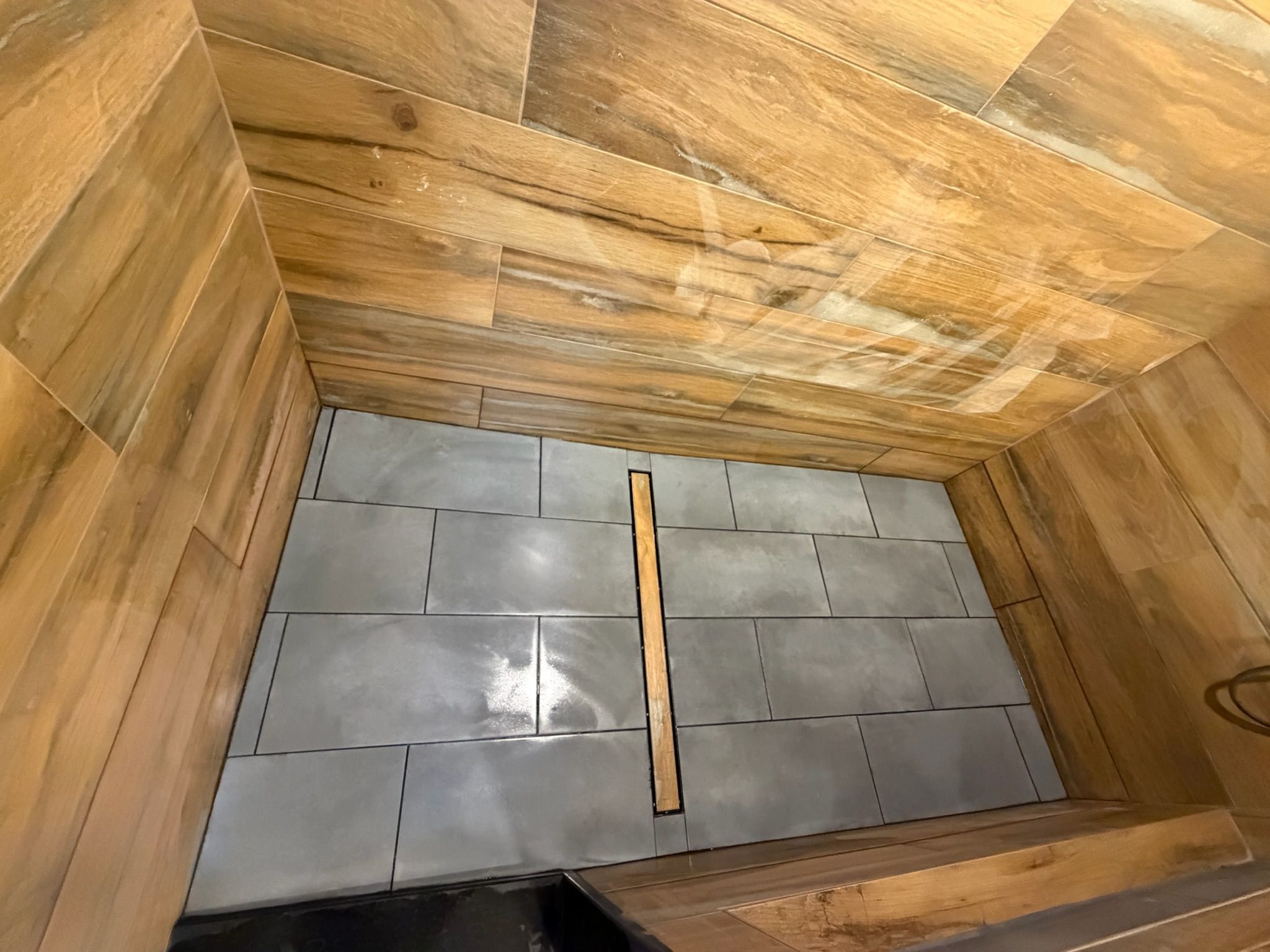 Modern shower with wood-look tile walls and gray slate floor tiles featuring a linear drain.