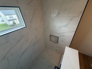 Walk-in shower detail showing white Calacatta porcelain wall tiles, built-in niche, and pebble tile shower floor.