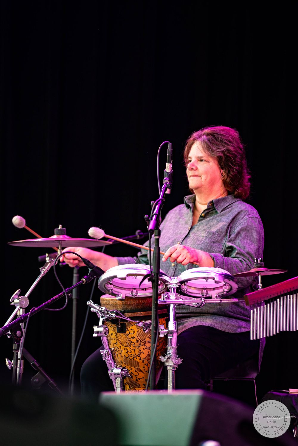 Musician playing drums and cymbals on stage under purple stage lighting during a live performance.