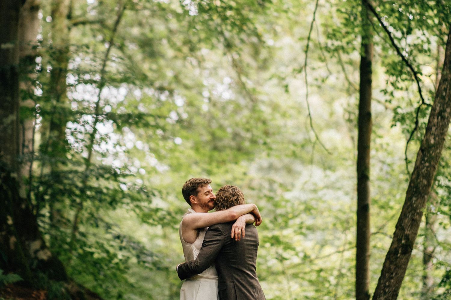 Couple embracing tenderly in a lush green forest during an outdoor wedding ceremony.