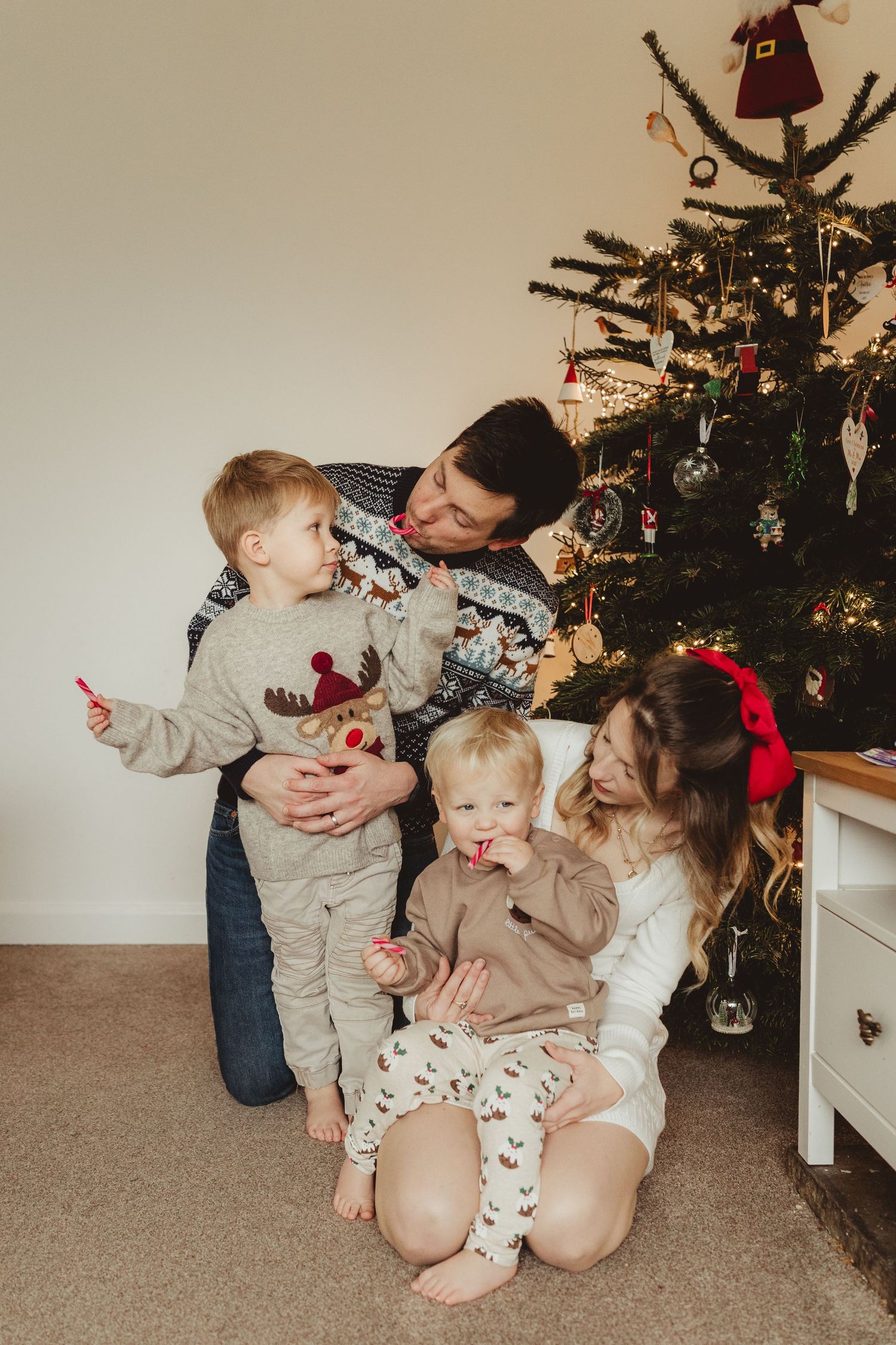 Family of four in Christmas sweaters gathered around a decorated tree, sharing candy canes on Christmas morning.