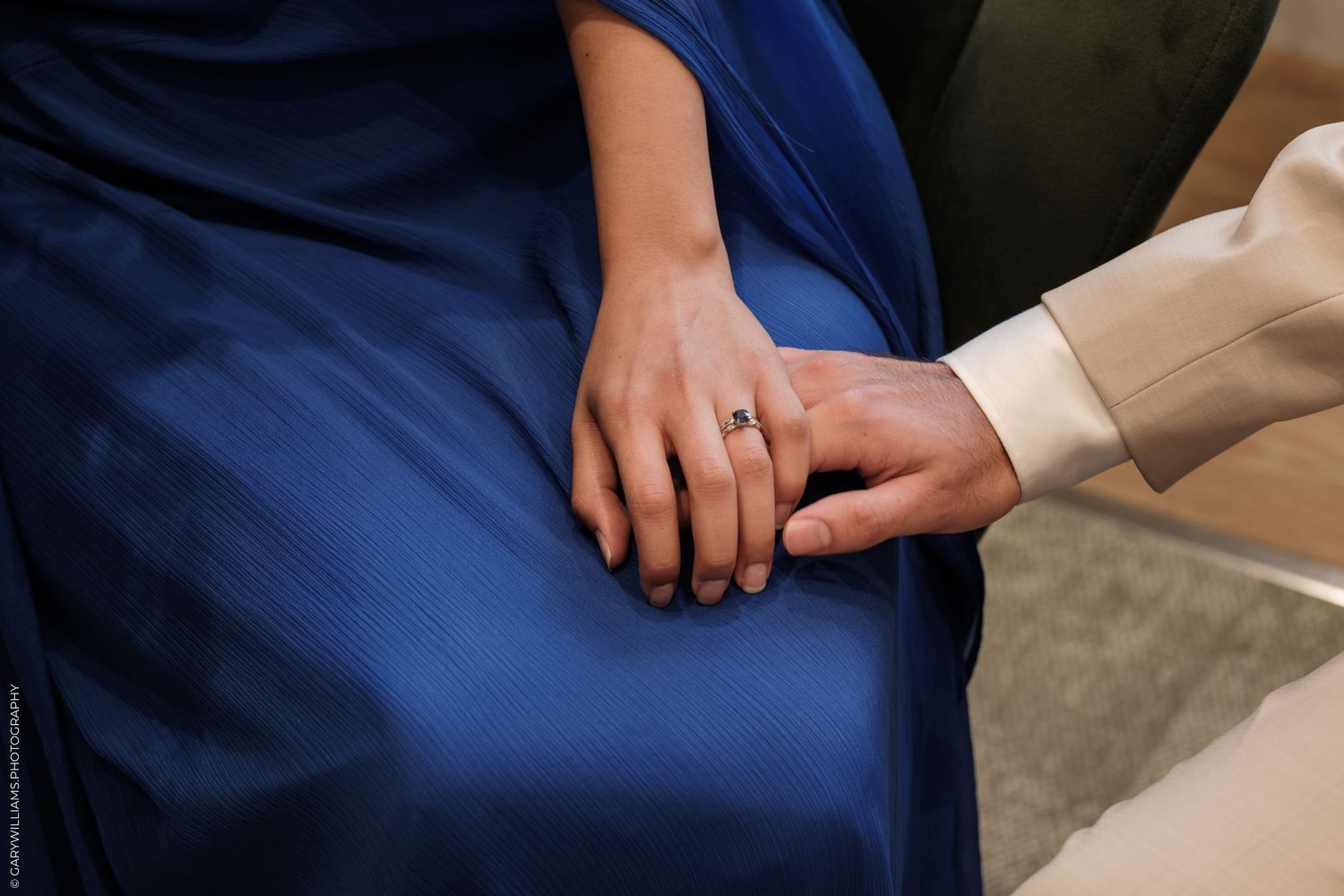 Close-up of two hands gently touching, woman wearing blue dress with elegant ring, romantic engagement moment.