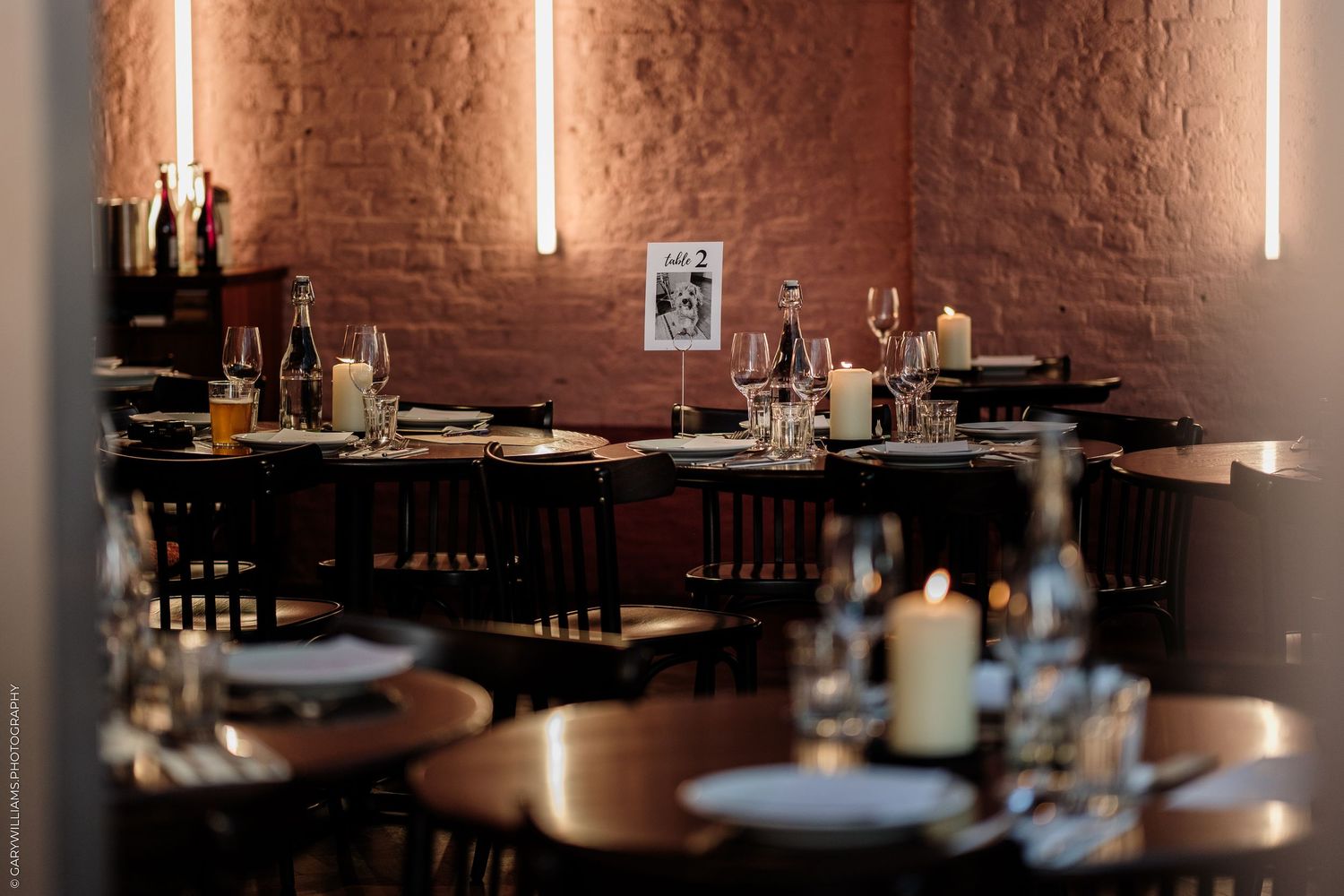 Elegant restaurant interior with candlelit tables, wine glasses, and warm brick walls creating a cozy dining atmosphere.