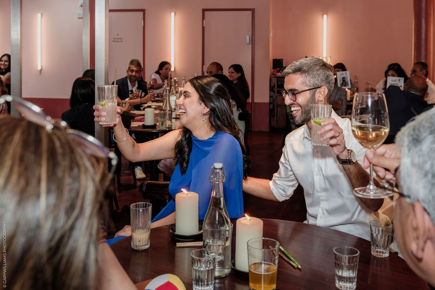 People toasting with wine glasses at a lively restaurant dinner party, smiling and celebrating together.
