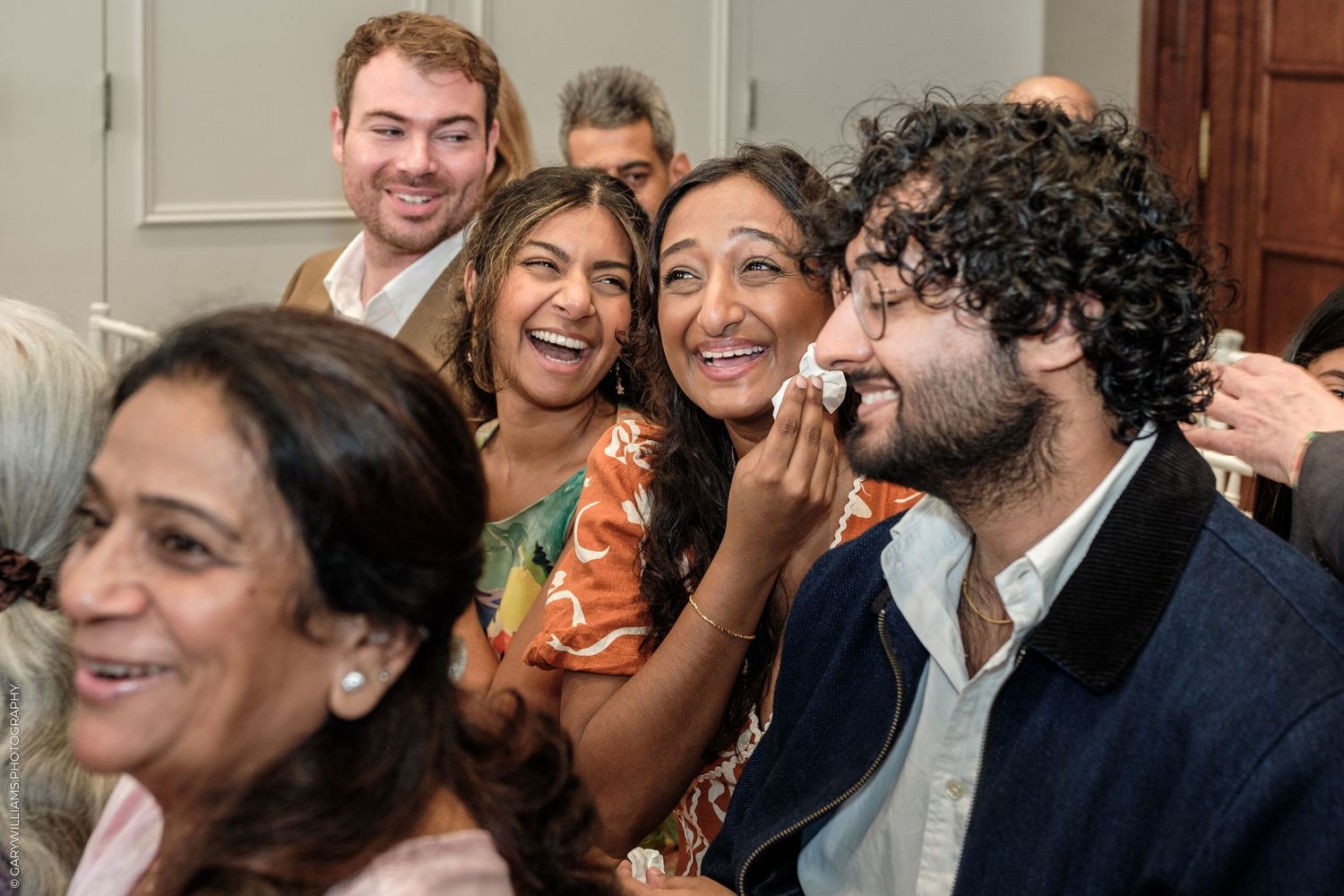 Diverse group of joyful people laughing together at a social gathering in a bright indoor setting.