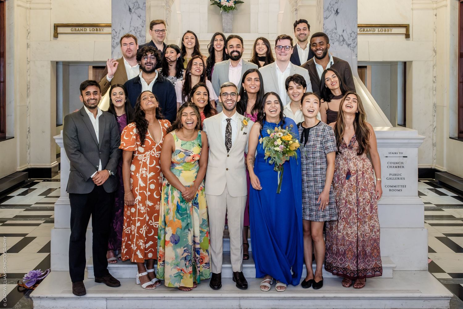 Large group of elegantly dressed people posing together on marble stairs at a wedding celebration.