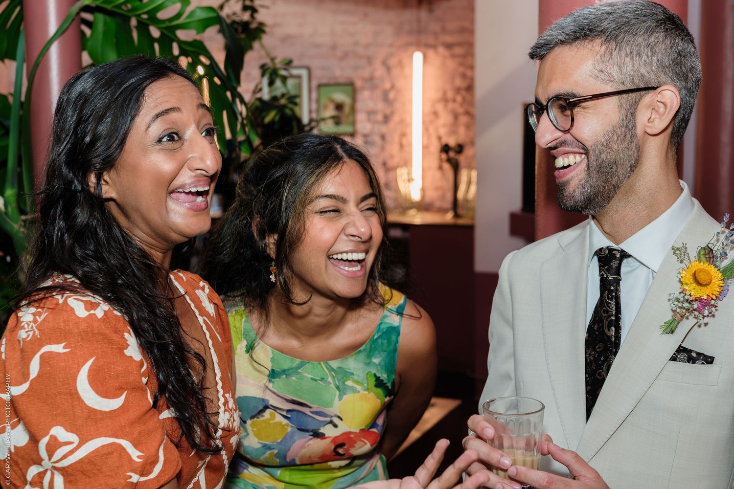 Three friends laughing and celebrating together at a festive party, with one man wearing a floral boutonniere.