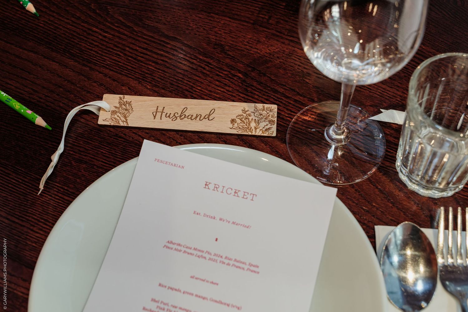 Elegant wedding table setting at Kricket restaurant with a wooden husband place card, white plate, and wine glass.
