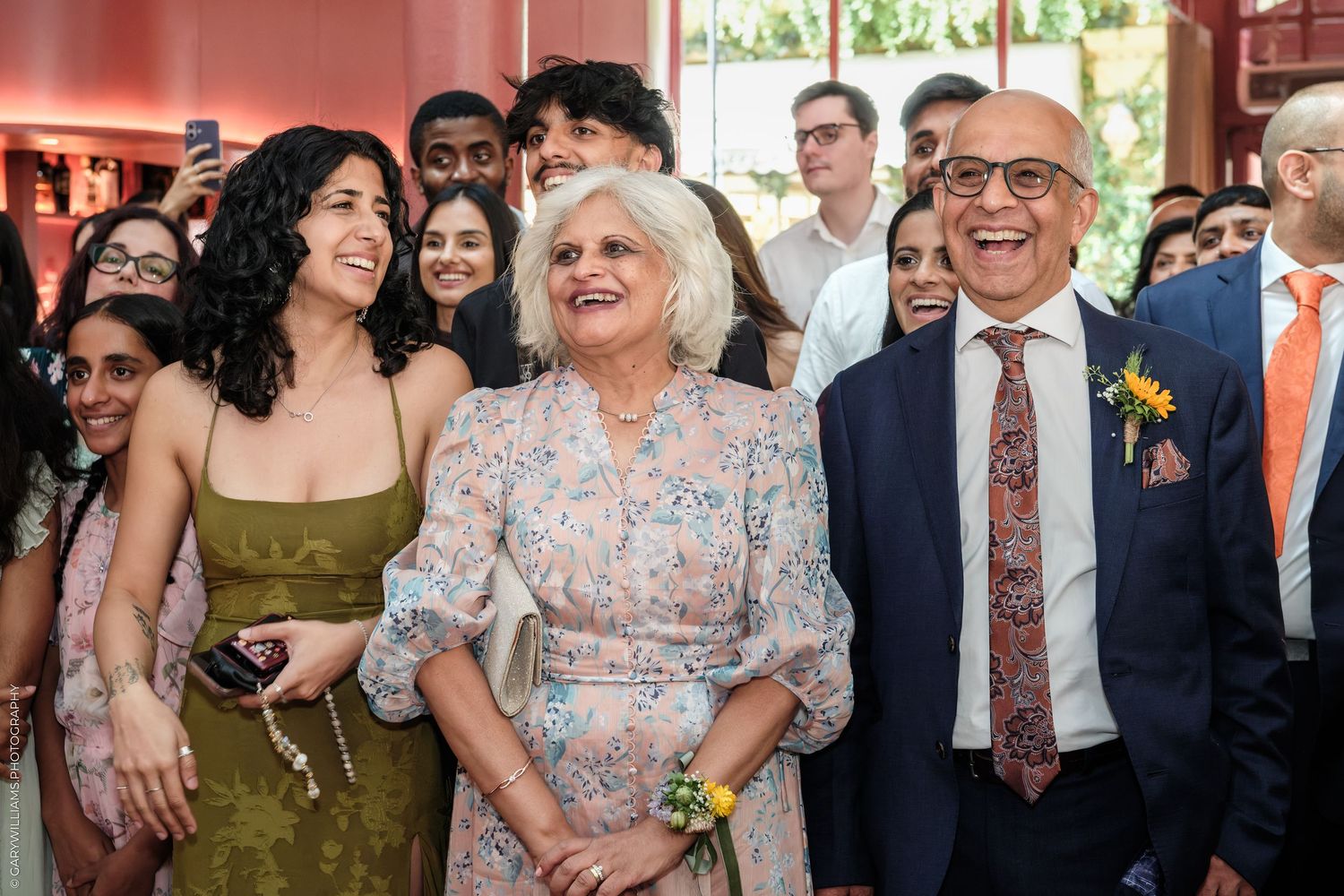 Group of smiling people posing together at a formal celebration, with a woman in floral dress at center.