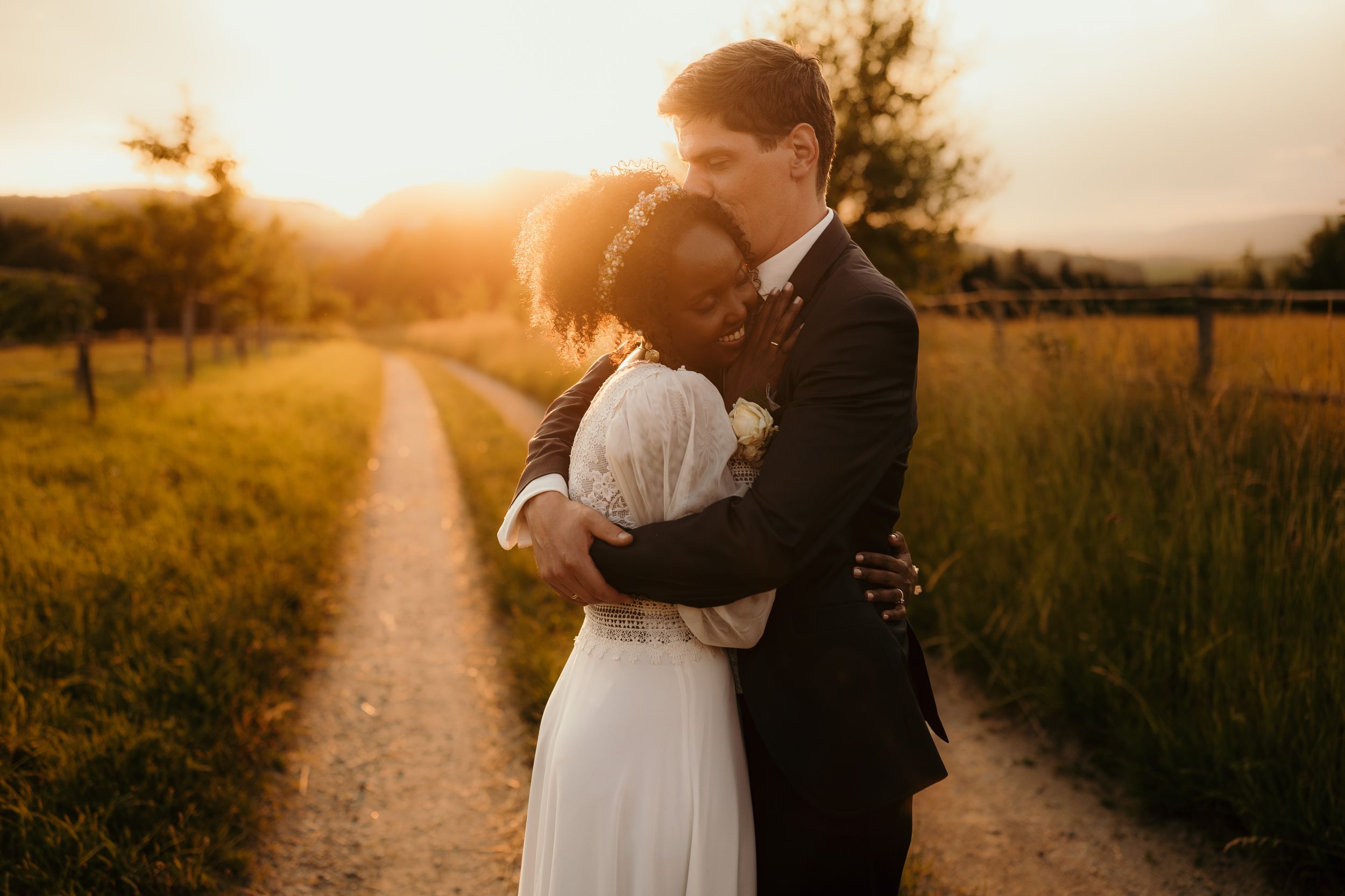 Romantic sunset portrait on dirt path with golden light filtering through summer grass.