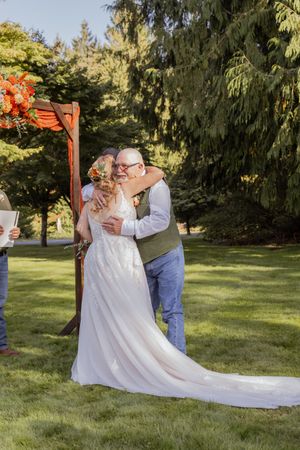 Bride and groom share a romantic first kiss embrace during outdoor wedding ceremony on lush green lawn.