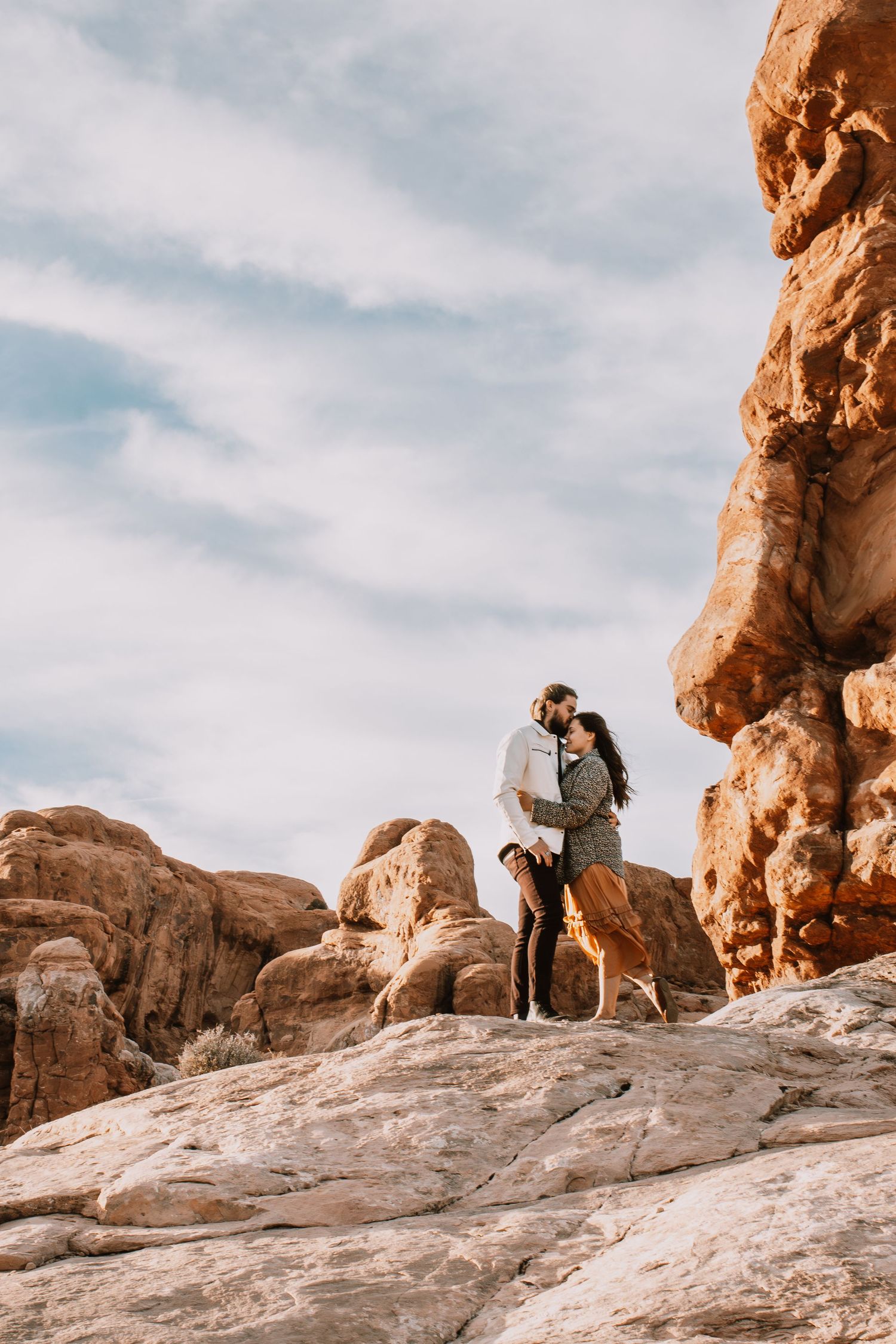 Couple embracing by large red rock formation in Moab, Utah