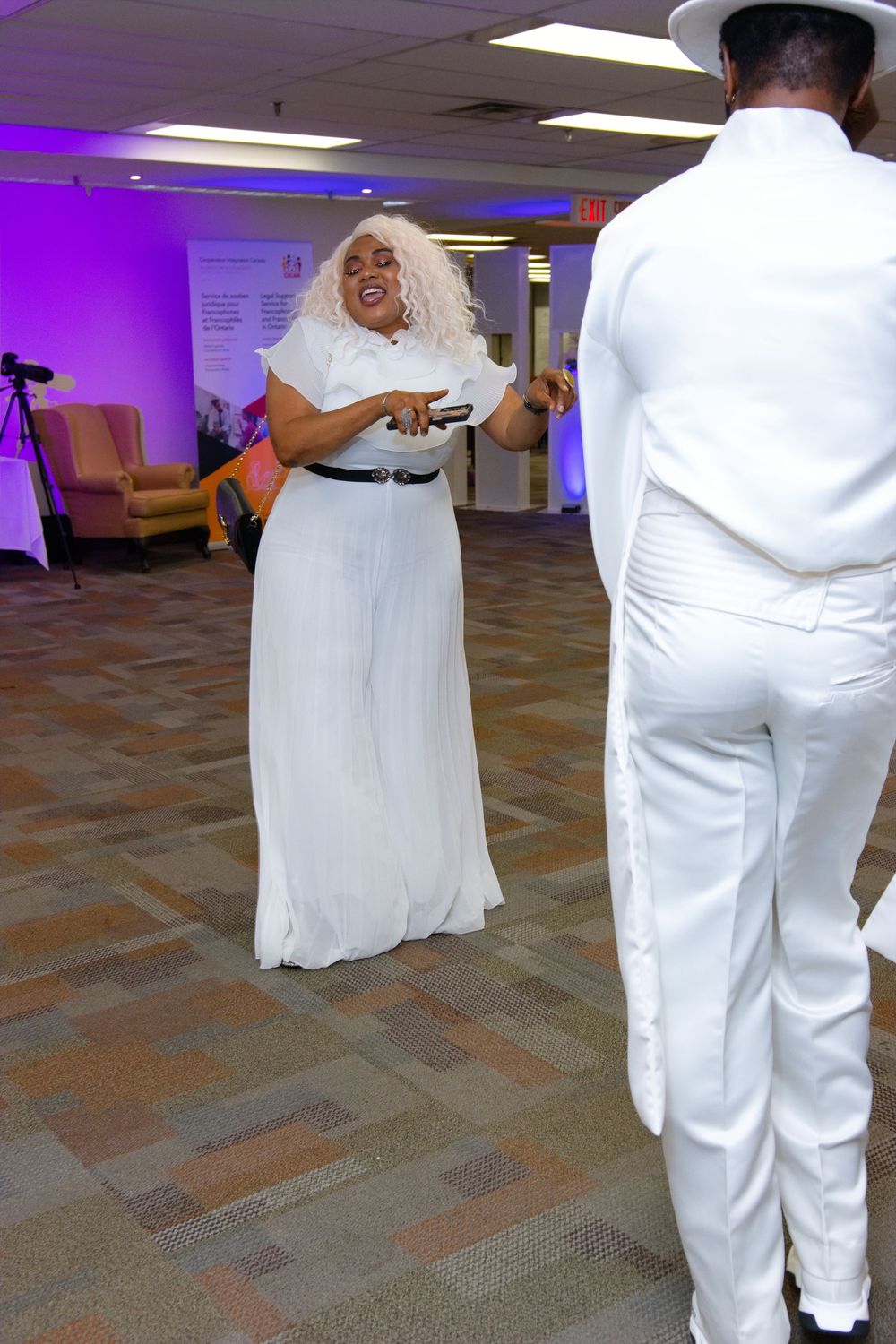 Two people dressed in white dancing at an indoor event with purple ambient lighting.