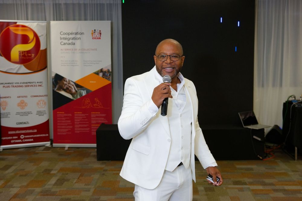 Man in white suit speaking into microphone at Cooperative Integration Canada event with promotional banners in background.