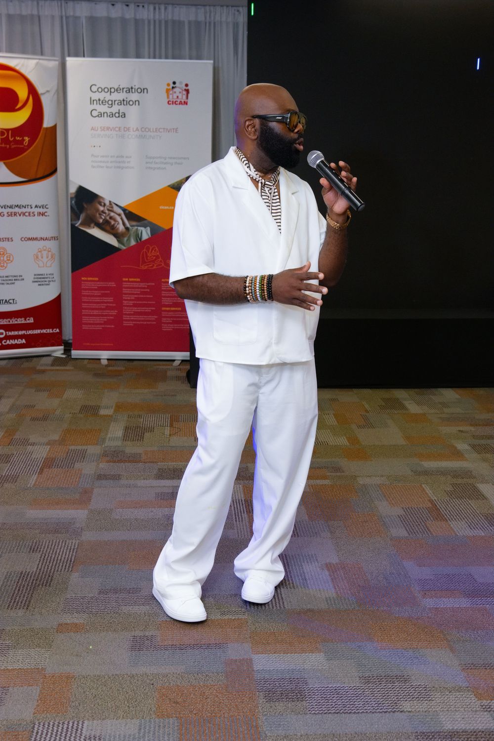 Man in white outfit singing into microphone at Coopération Intégration Canada event.