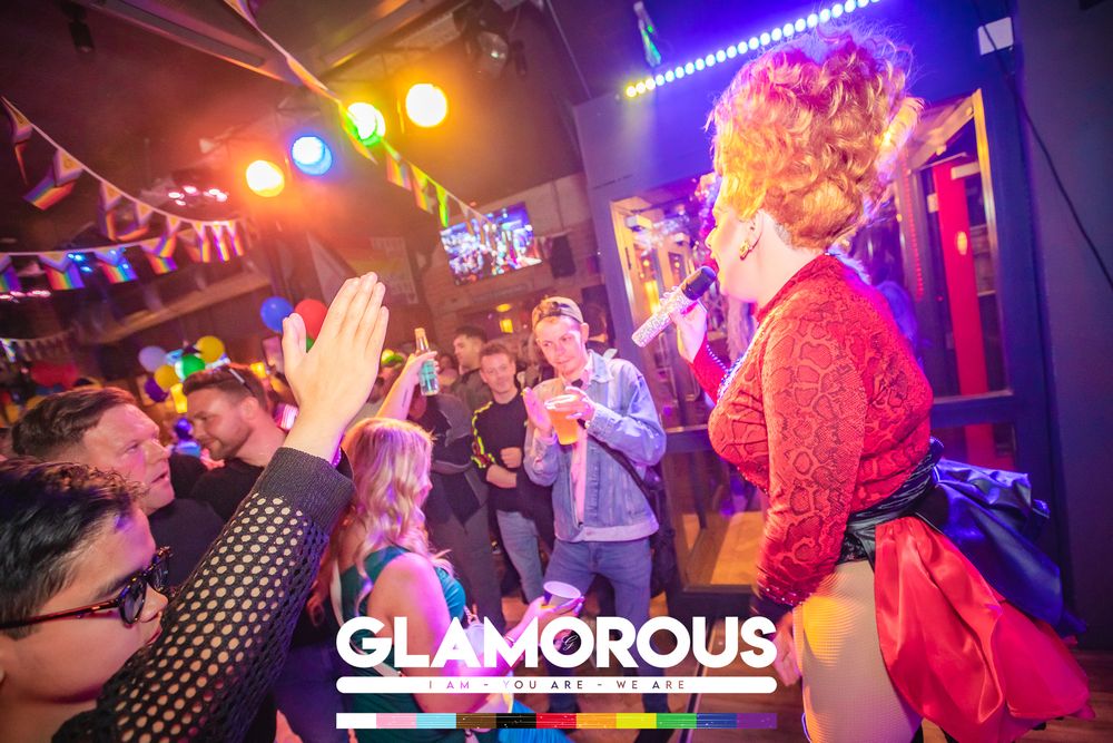 Lively drag performer entertaining crowd at Glamorous nightclub event with colorful lights and festive atmosphere.
