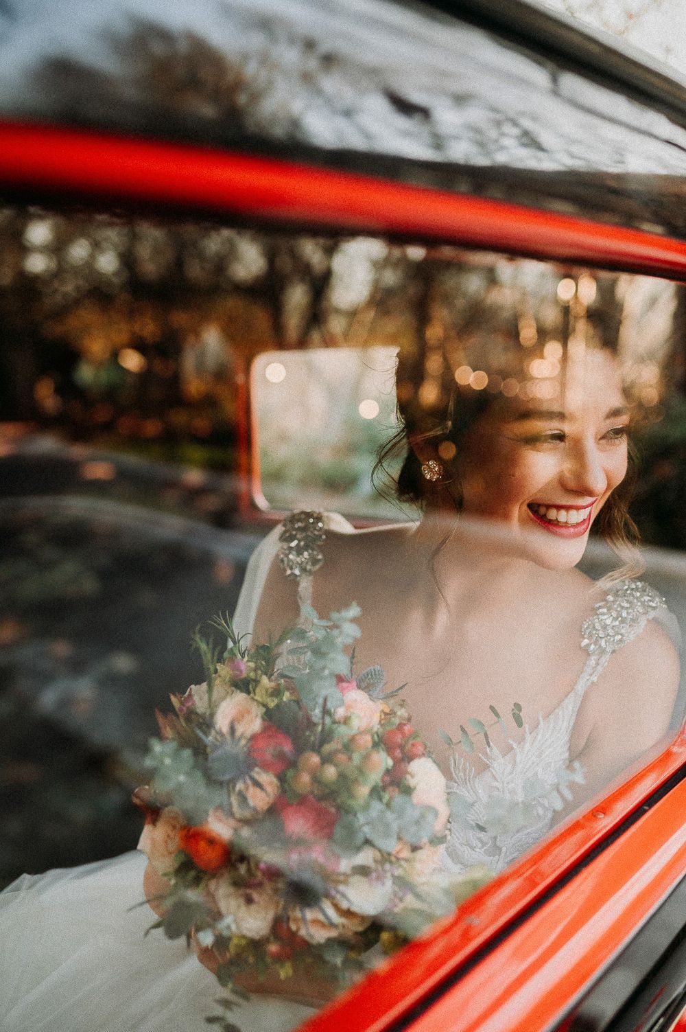 Black and white wedding photo of bride with bouquet, bridesmaid, and groom near elegant horse-drawn carriage outdoors.