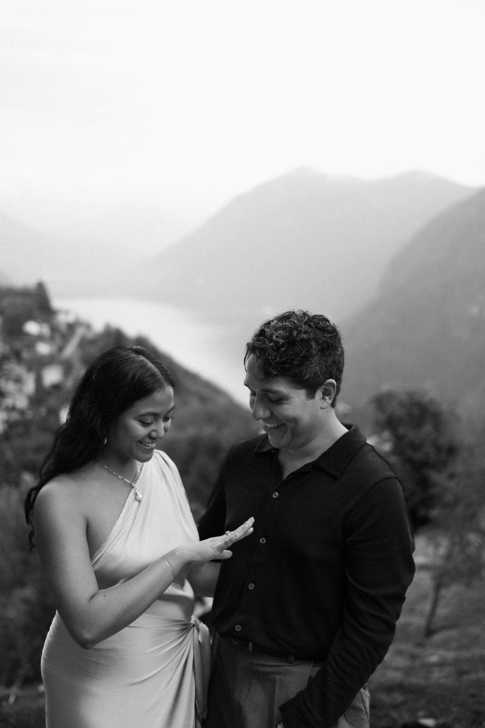 Black and white photo of a couple smiling together with mountain lake backdrop during engagement session.