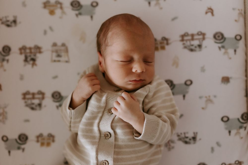 Peaceful newborn baby sleeping in a striped onesie on a white vehicle-print blanket.