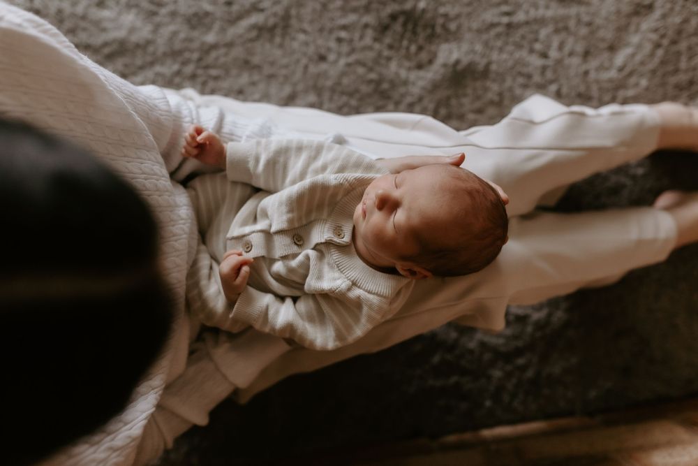 Newborn baby in white onesie lying on soft blanket, peaceful and serene in natural light photography.