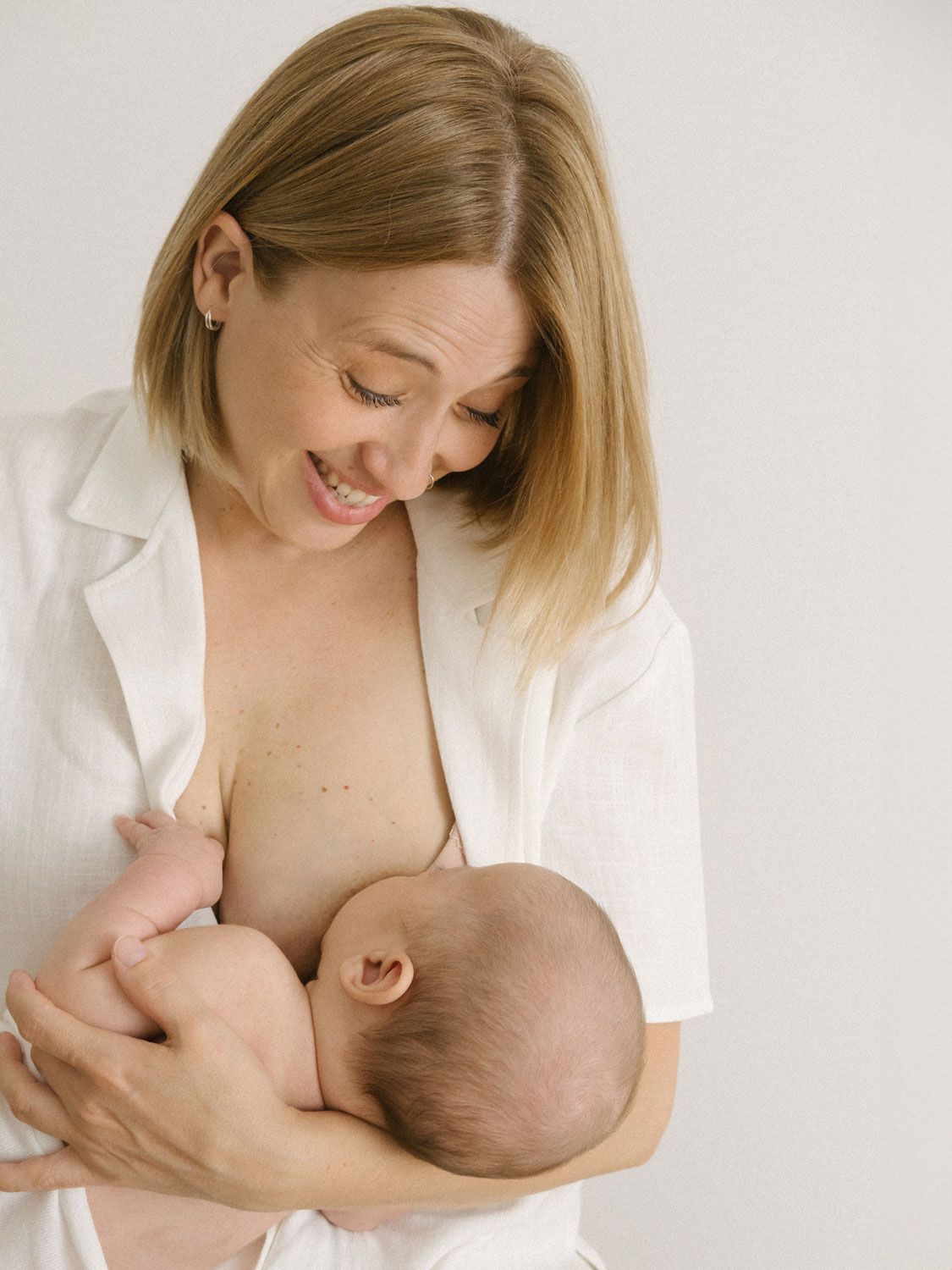 Momento íntimo de lactancia entre madre y bebé recién nacido mientras visten una camisa blanca.
