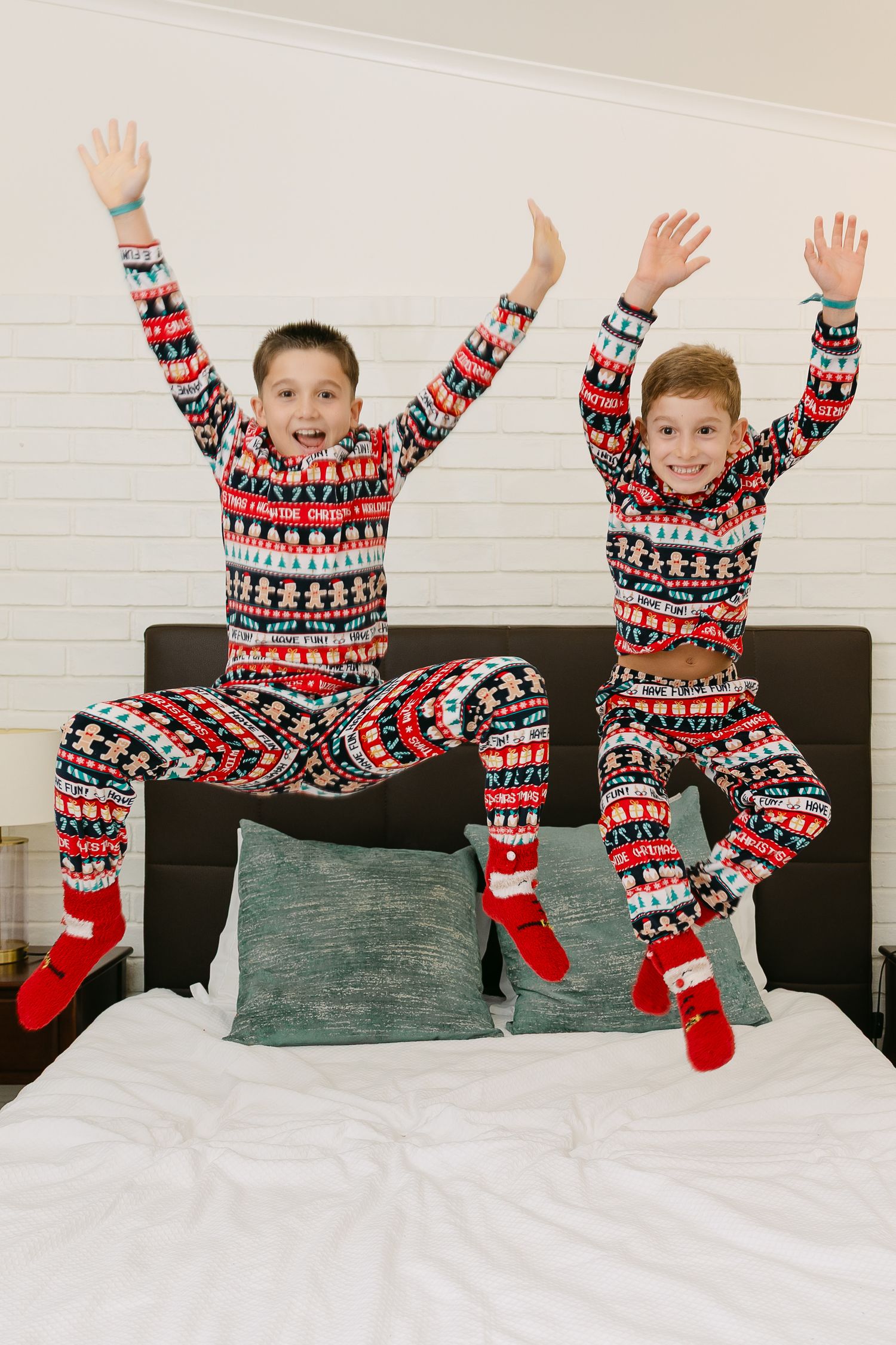 Child in red holiday outfit jumping playfully on white bedding with festive garland decor.
