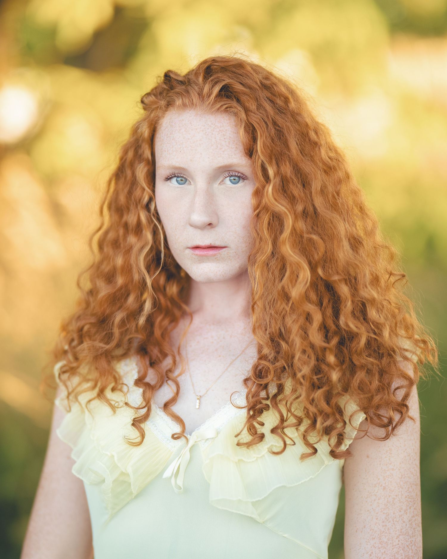 Young woman with long curly red hair and blue eyes wearing a light green dress outdoors.