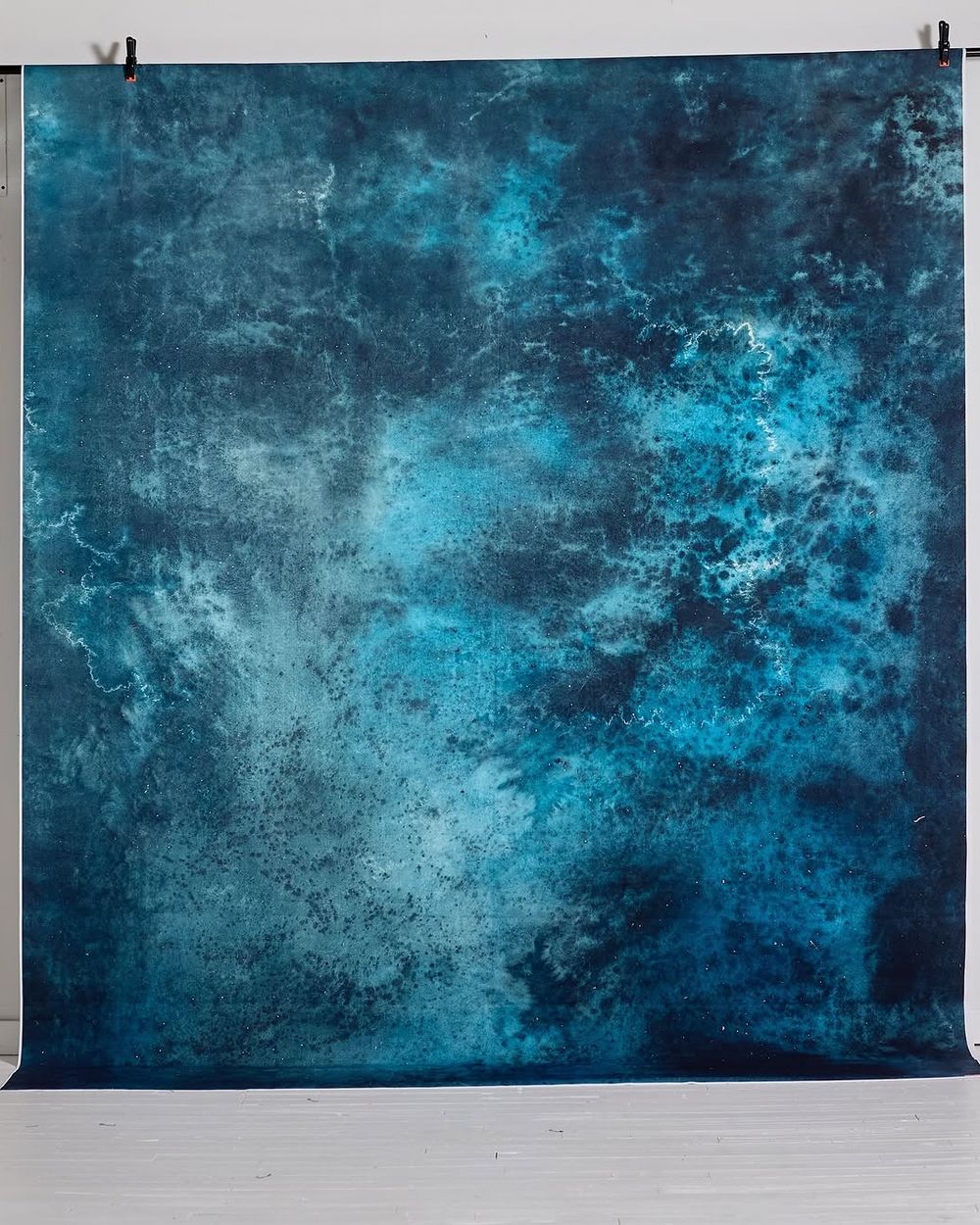 Abstract teal and dark blue textured photography backdrop with weathered paint effect hanging in studio.
