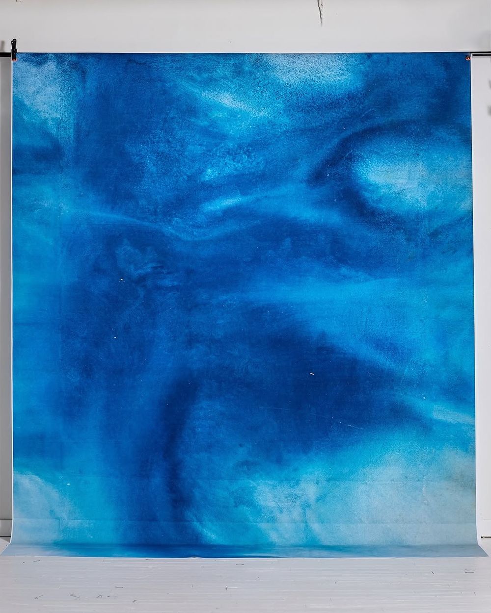 Vibrant blue watercolor-style swirling abstract photography backdrop displayed in a white studio setting.