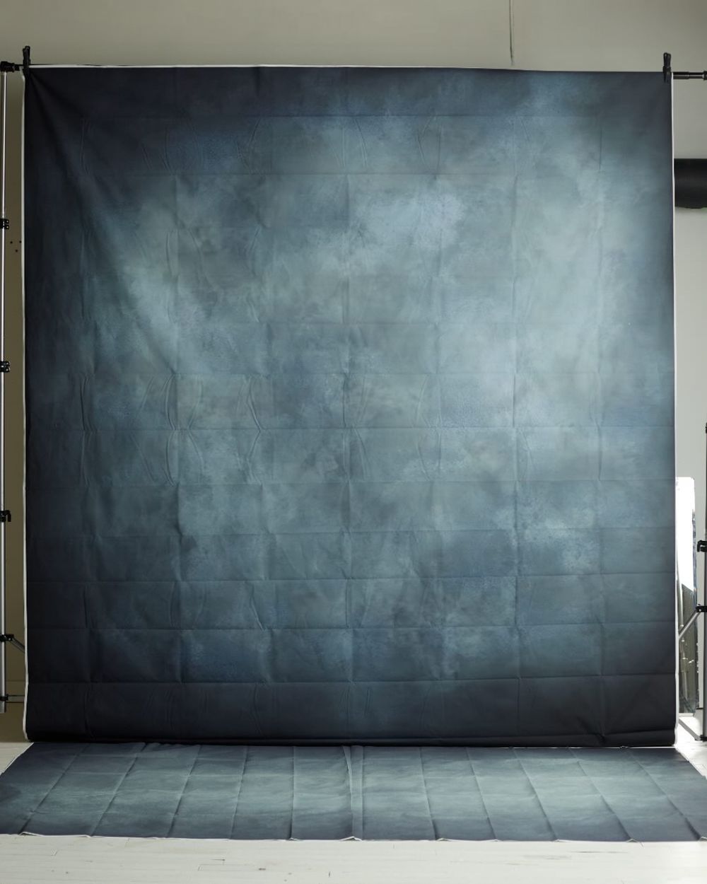 Dark slate blue abstract textured photography backdrop with subtle cloud-like tones displayed in a bright studio.