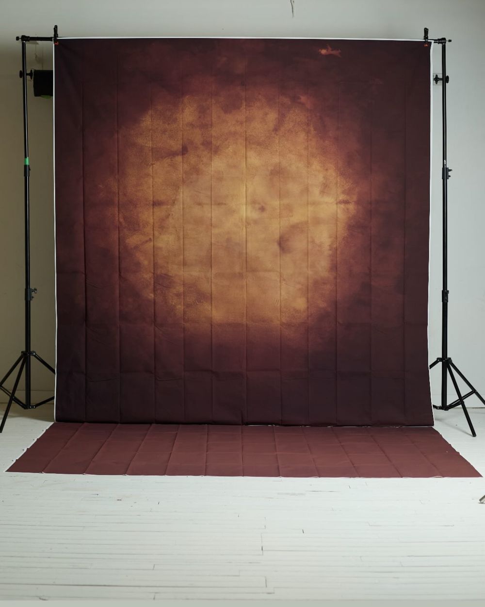 Dark brown and golden abstract photography backdrop on a stand in a white studio.