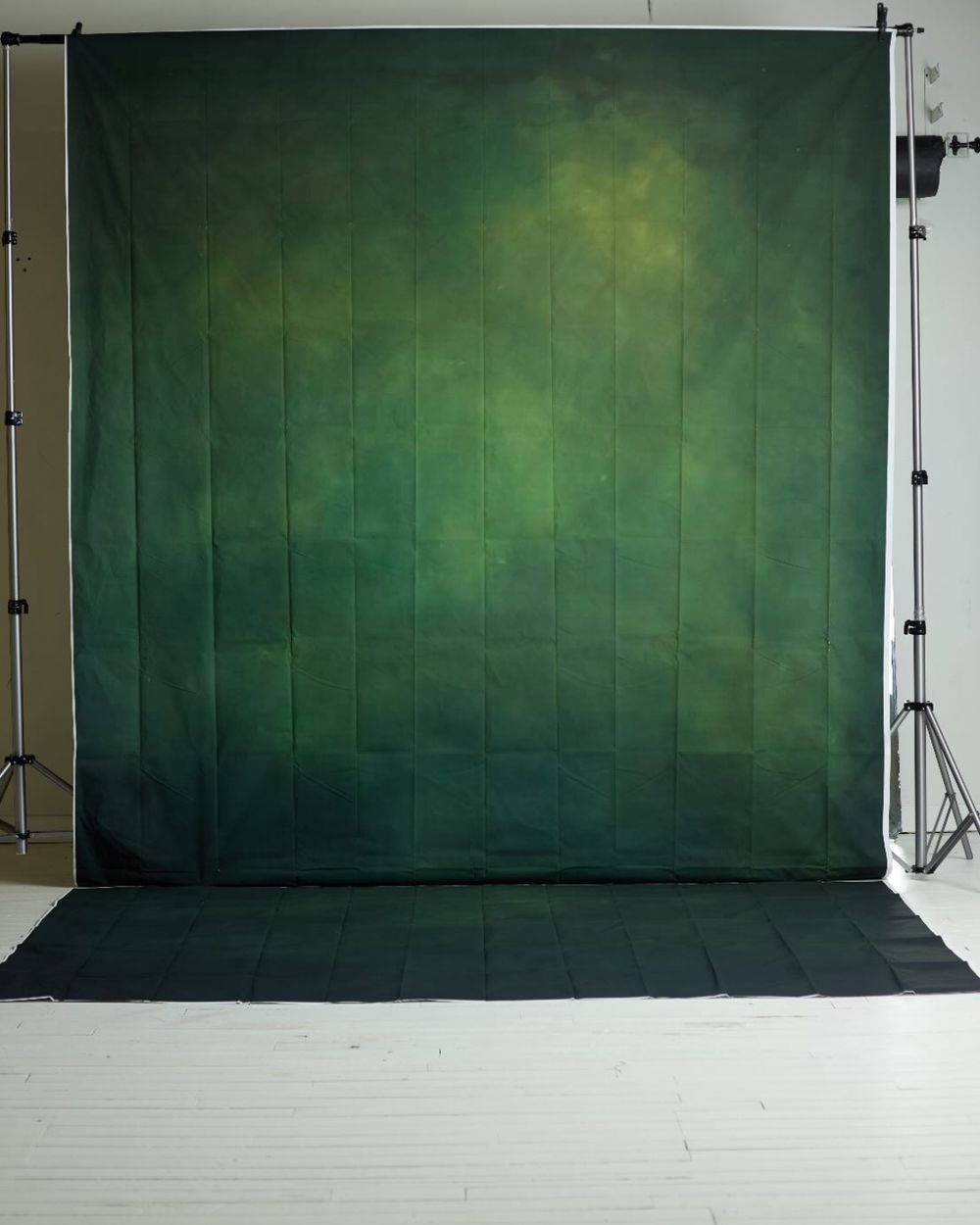 Deep green textured photography backdrop on a stand in a bright white studio.