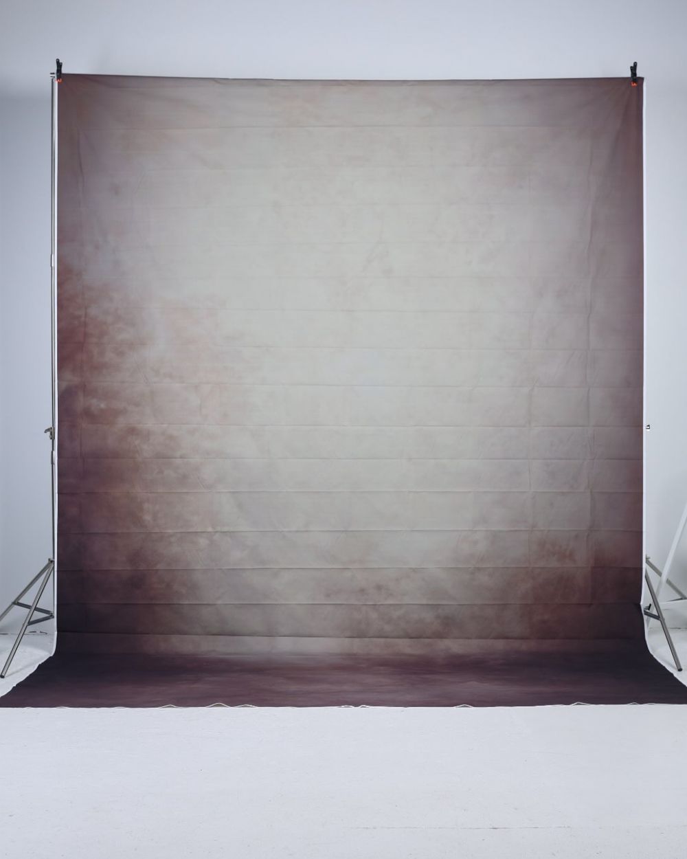 Light gray and brown gradient photography backdrop on a stand in a white studio.