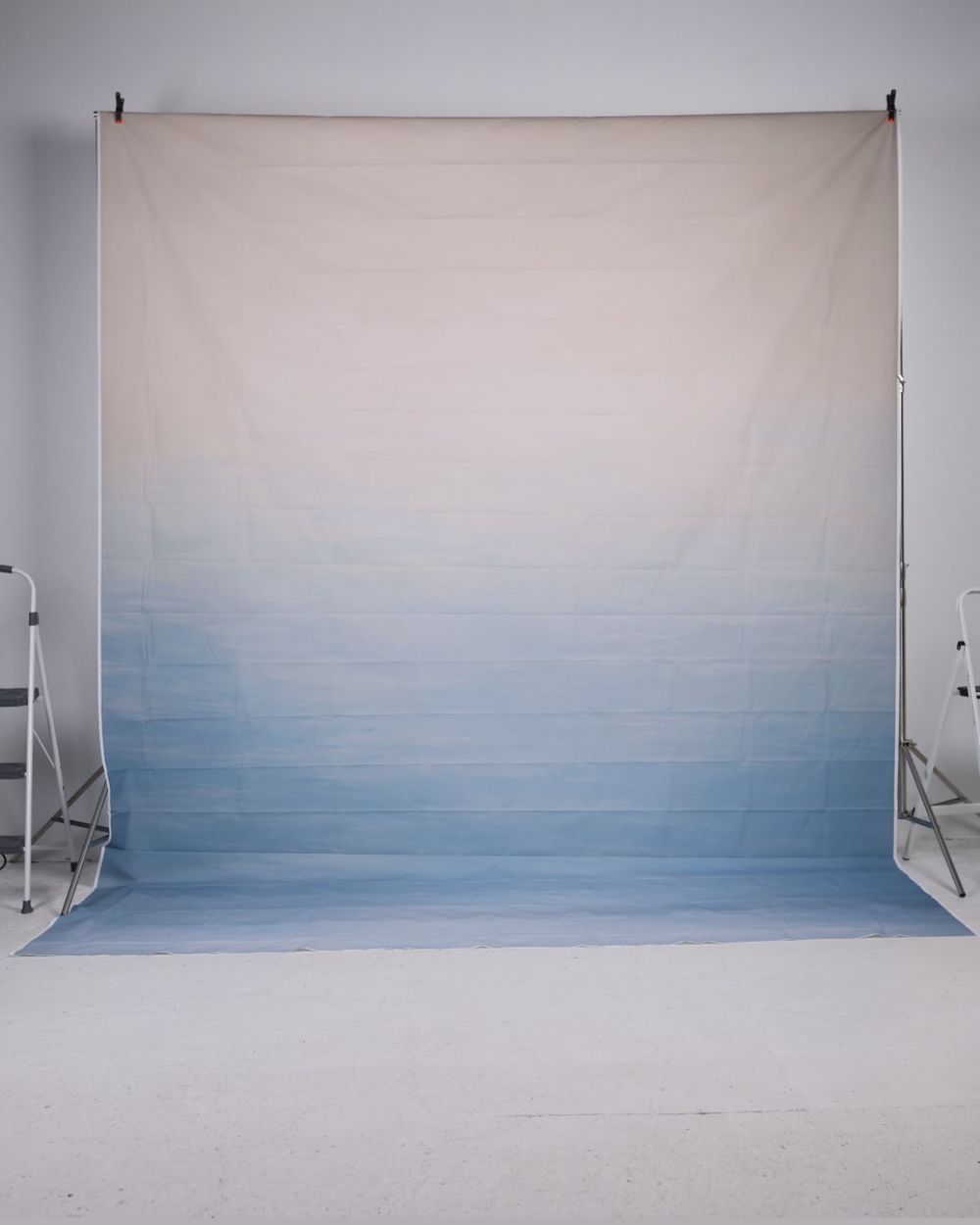 White to blue ombre gradient photography backdrop on a stand in a white studio.