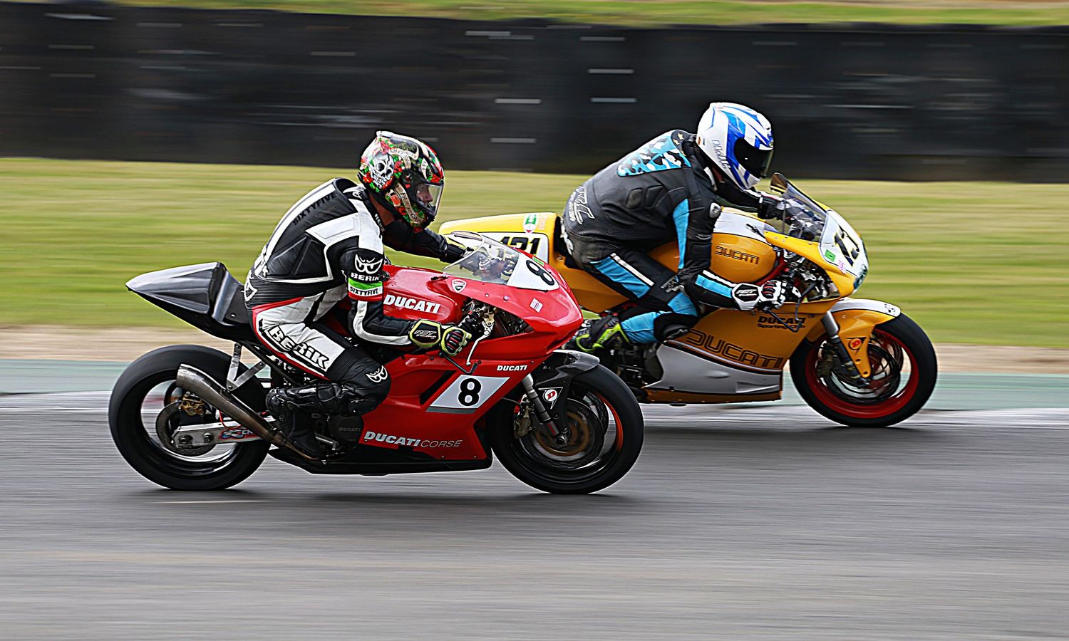 Two motorcycles racing on a track, red Ducati number 8 and yellow bike competing.