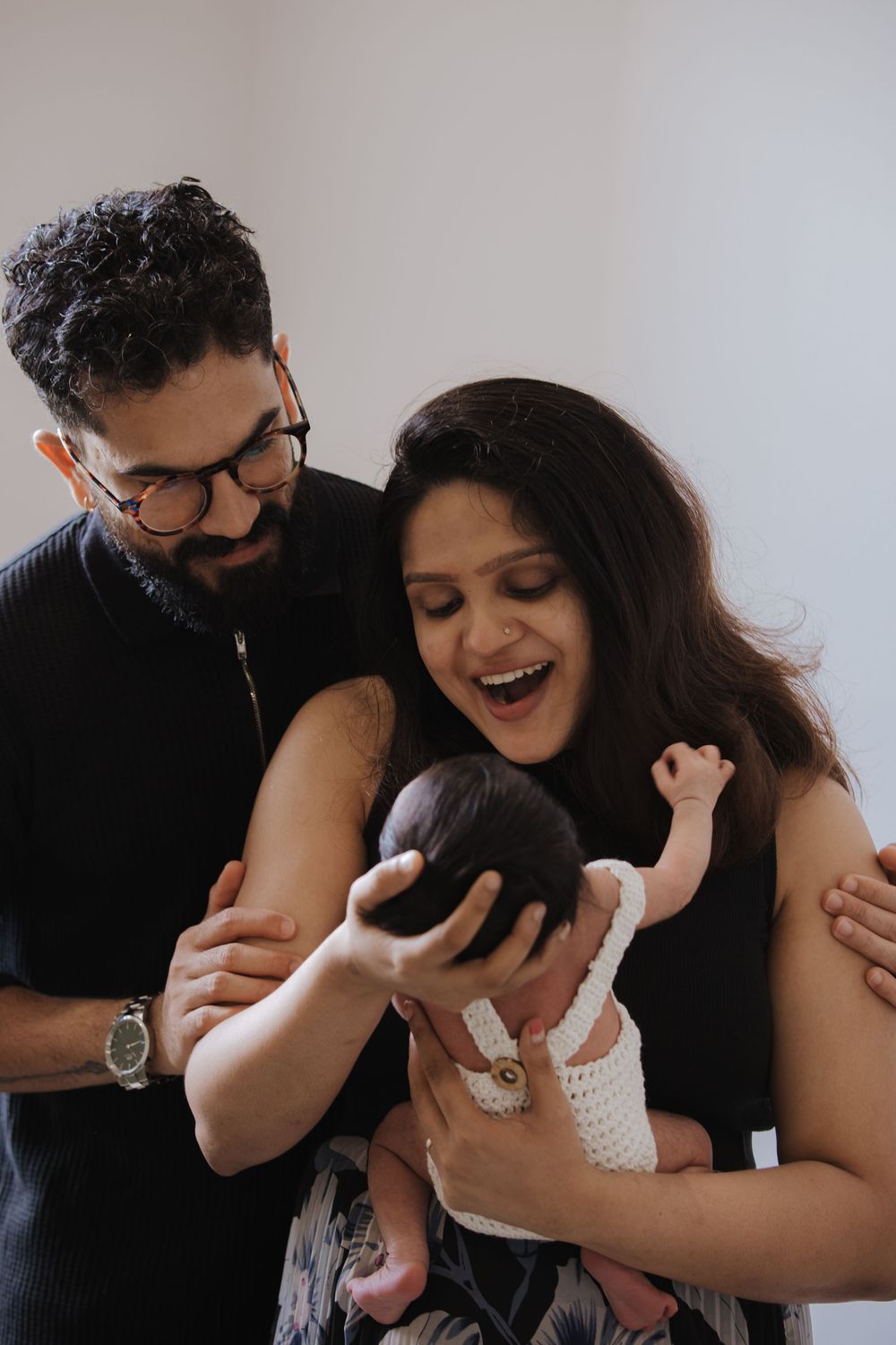 Joyful parents admiring their newborn baby dressed in white crochet outfit.