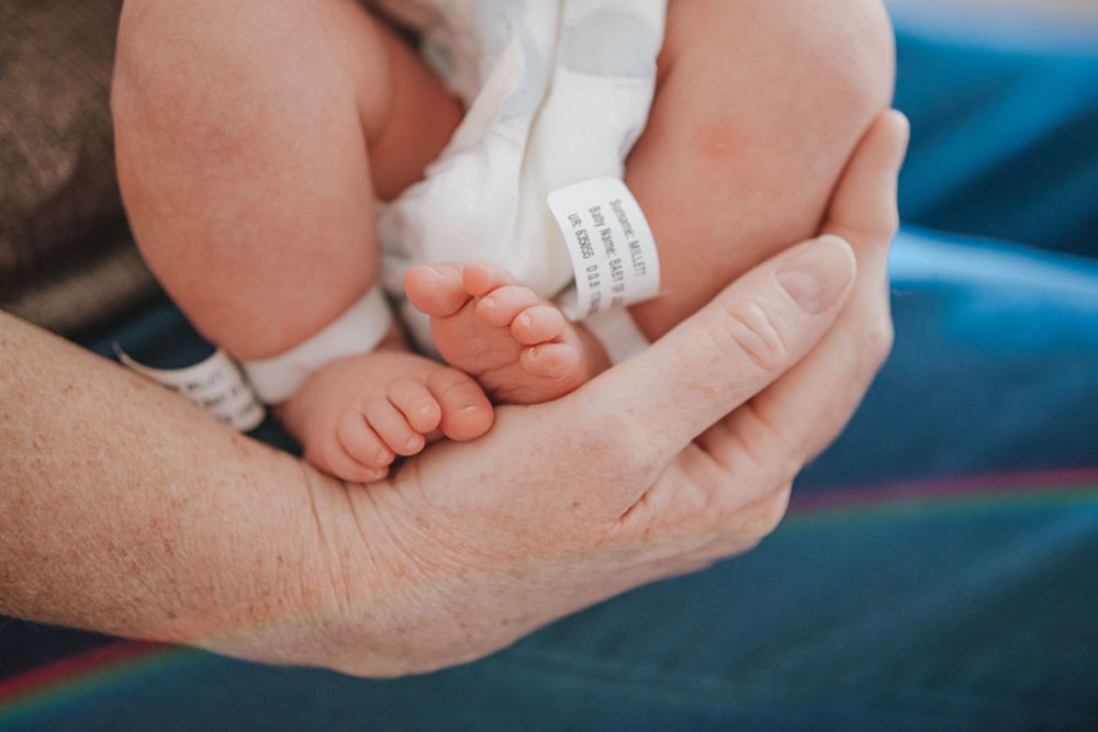 Newborn baby feet resting in a grandparent's hand with hospital identification bracelet.