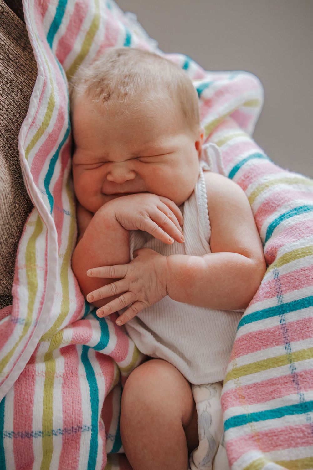 Sleeping newborn baby wrapped in colorful striped blanket, curled up peacefully.