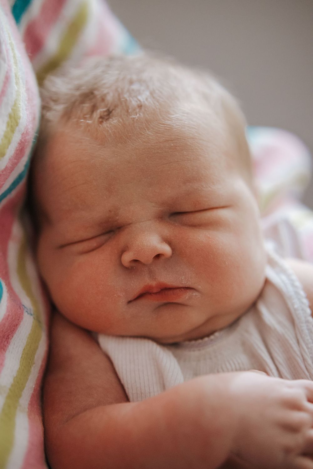 Peaceful sleeping newborn baby with chubby cheeks resting on a colorful striped blanket.