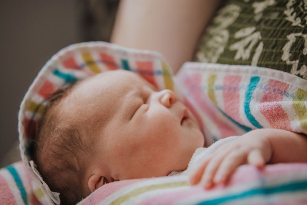 Newborn baby sleeping peacefully wrapped in a colorful striped blanket cradled in an adult's arms.