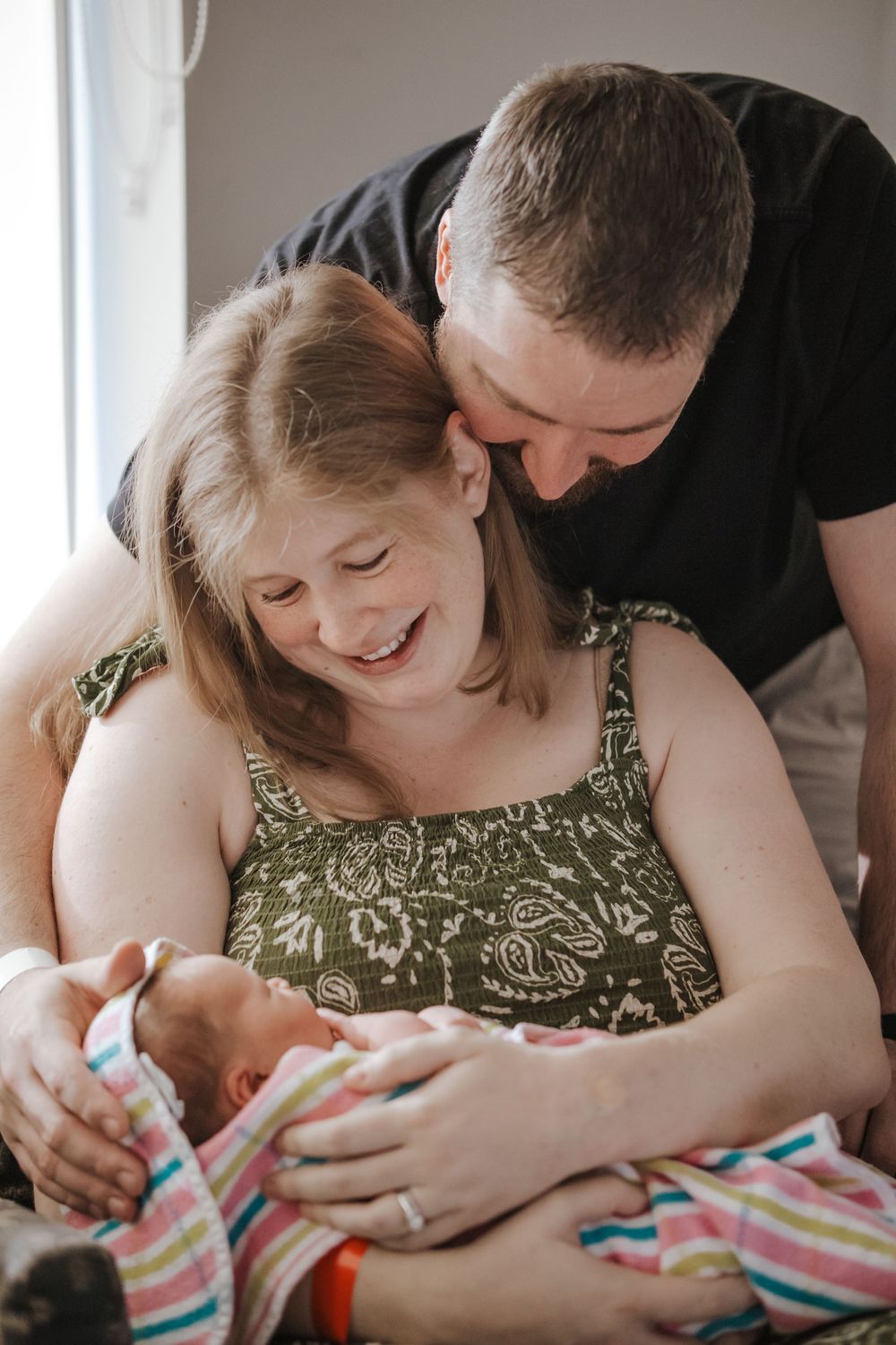 Happy couple smiling and bonding with their newborn baby wrapped in a colorful striped blanket during fresh 48 newborn photos.
