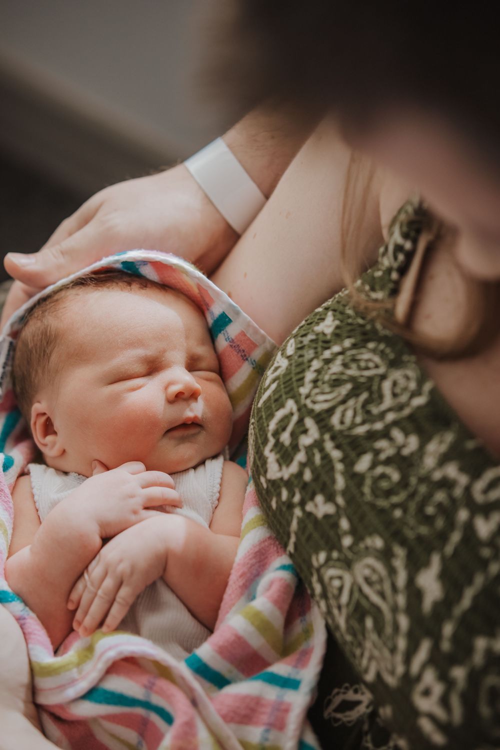Newborn baby sleeping peacefully in colorful striped blanket, cradled in mother's arms at hospital.