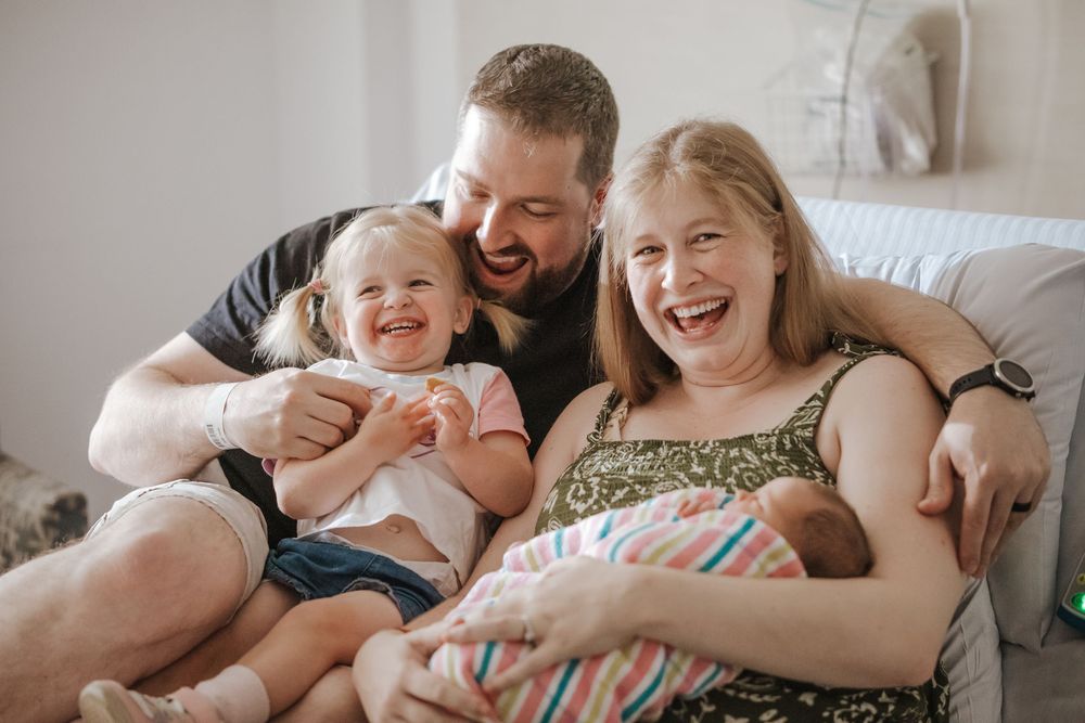 Happy family laughing together holding newborn baby and toddler at home.