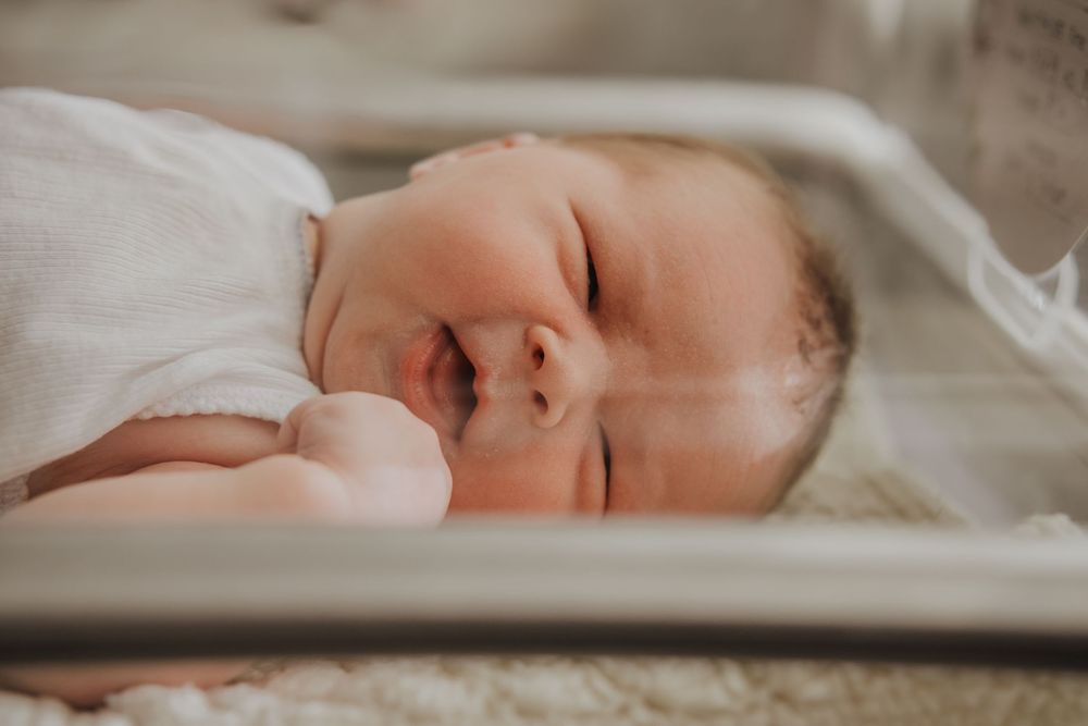 Newborn baby sleeping peacefully in a hospital bassinet, wrapped in a white swaddle blanket.