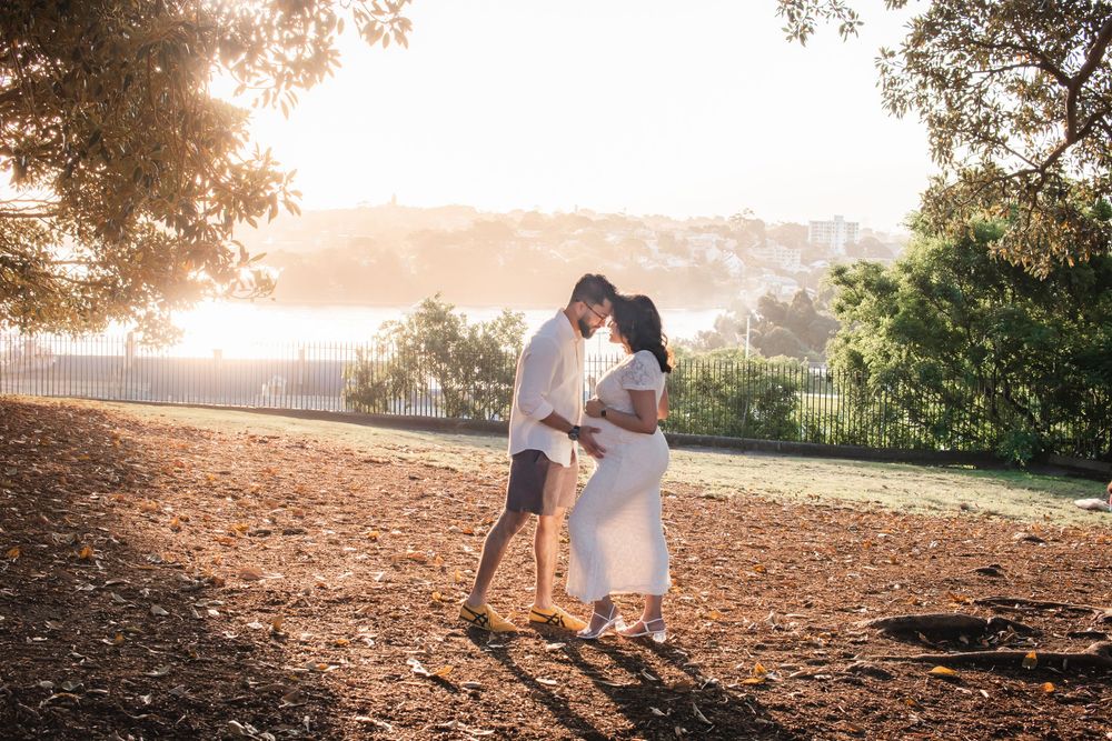 Couple sharing a romantic kiss at golden hour in an open field surrounded by trees and warm sunlight.
