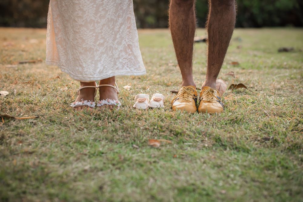Couple standing on grass with tiny baby shoes between their feet, pregnancy announcement photo.