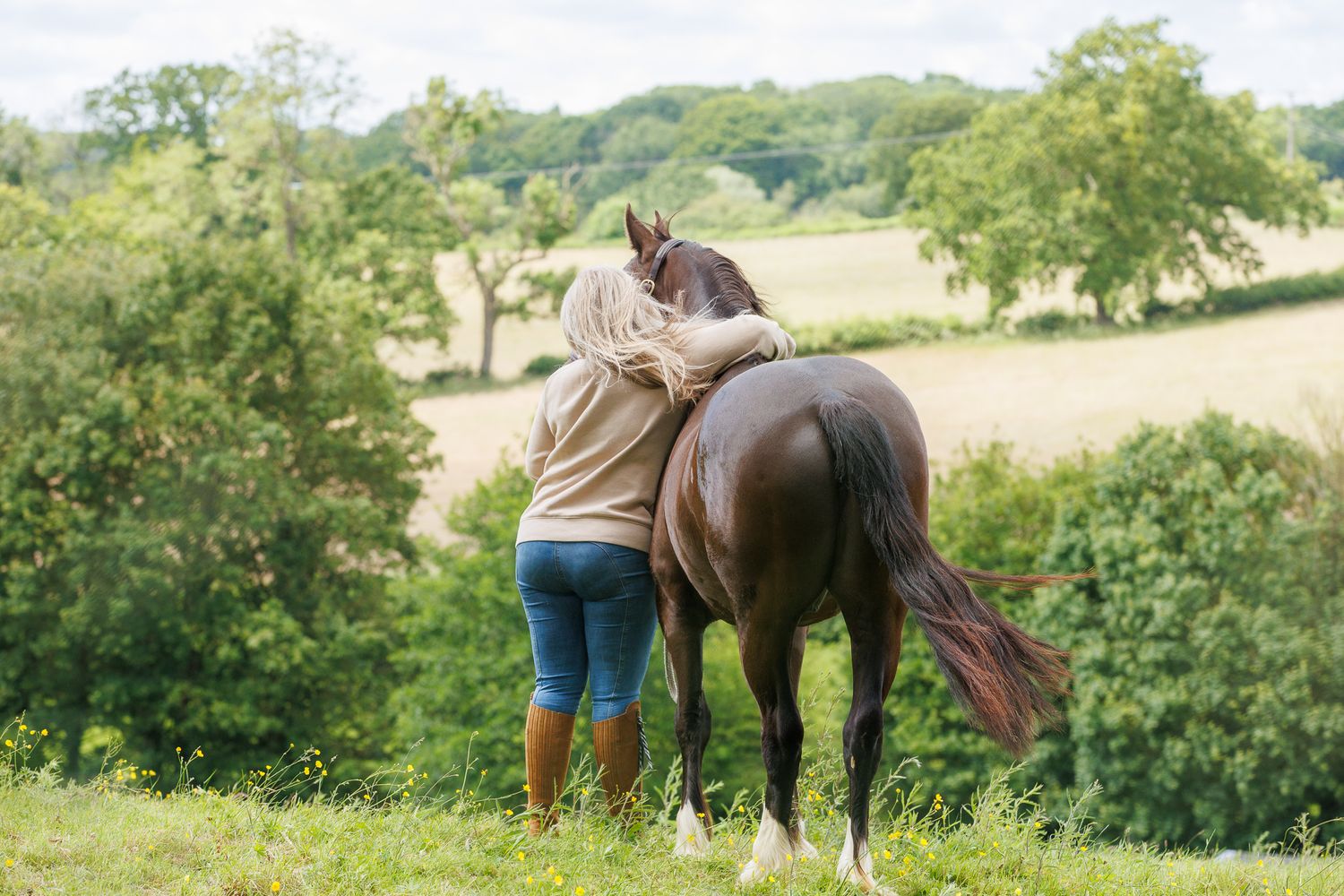 Woman leading a dark brown horse along a lush green garden path beside a tranquil pond.